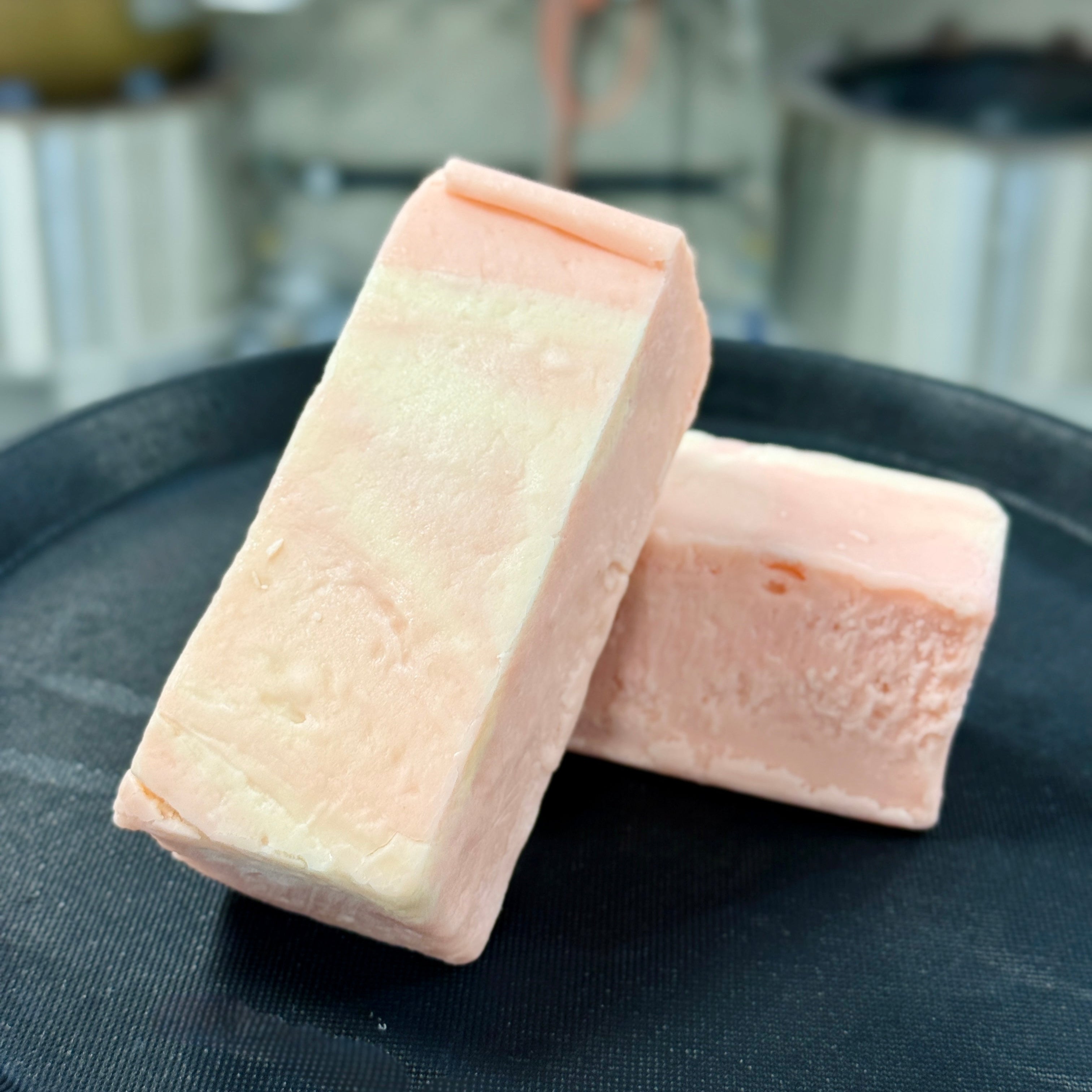 Two blocks of strawberries & cream fudge on a black surface with a blurred kitchen background