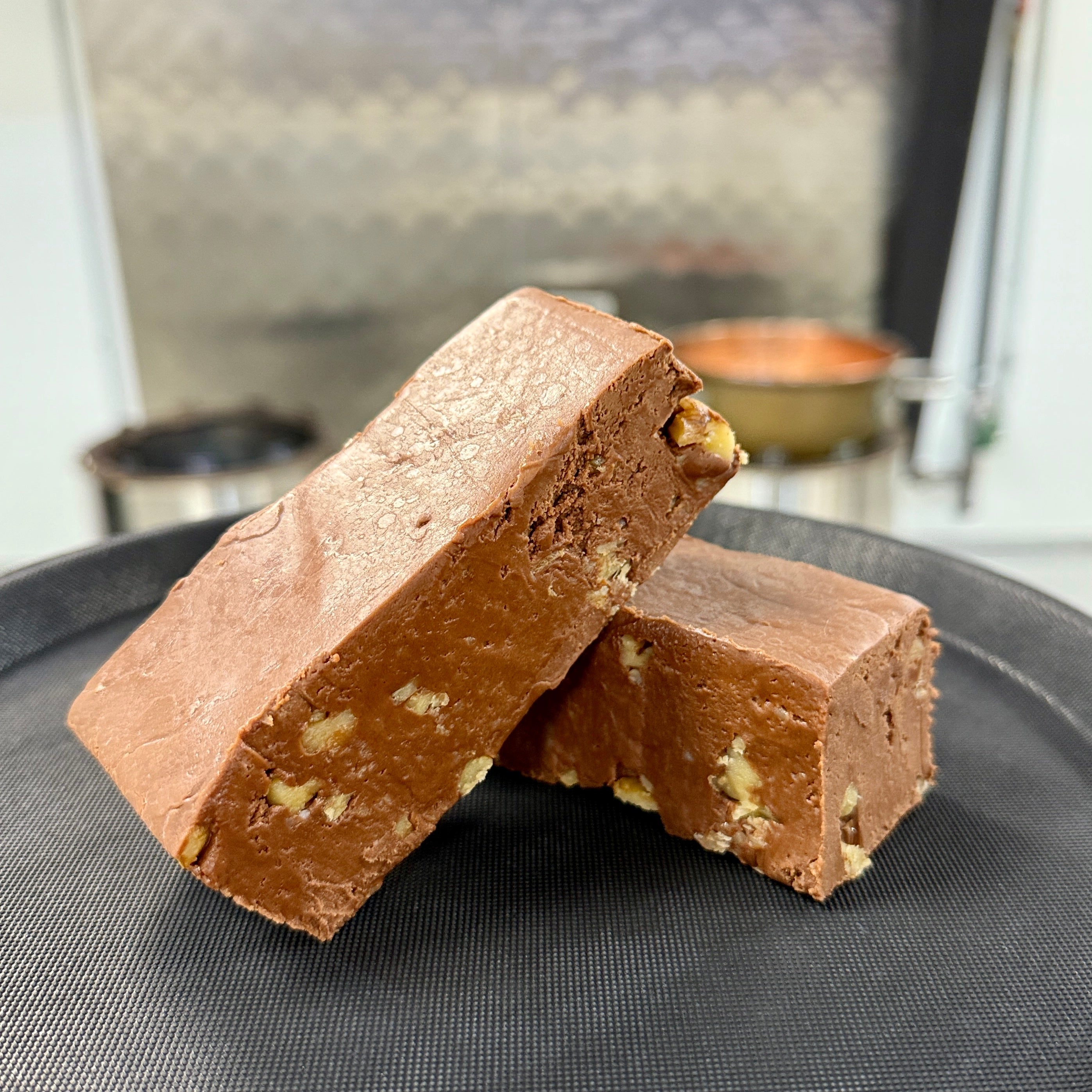 Two pieces of chocolate fudge with nuts on a black plate.