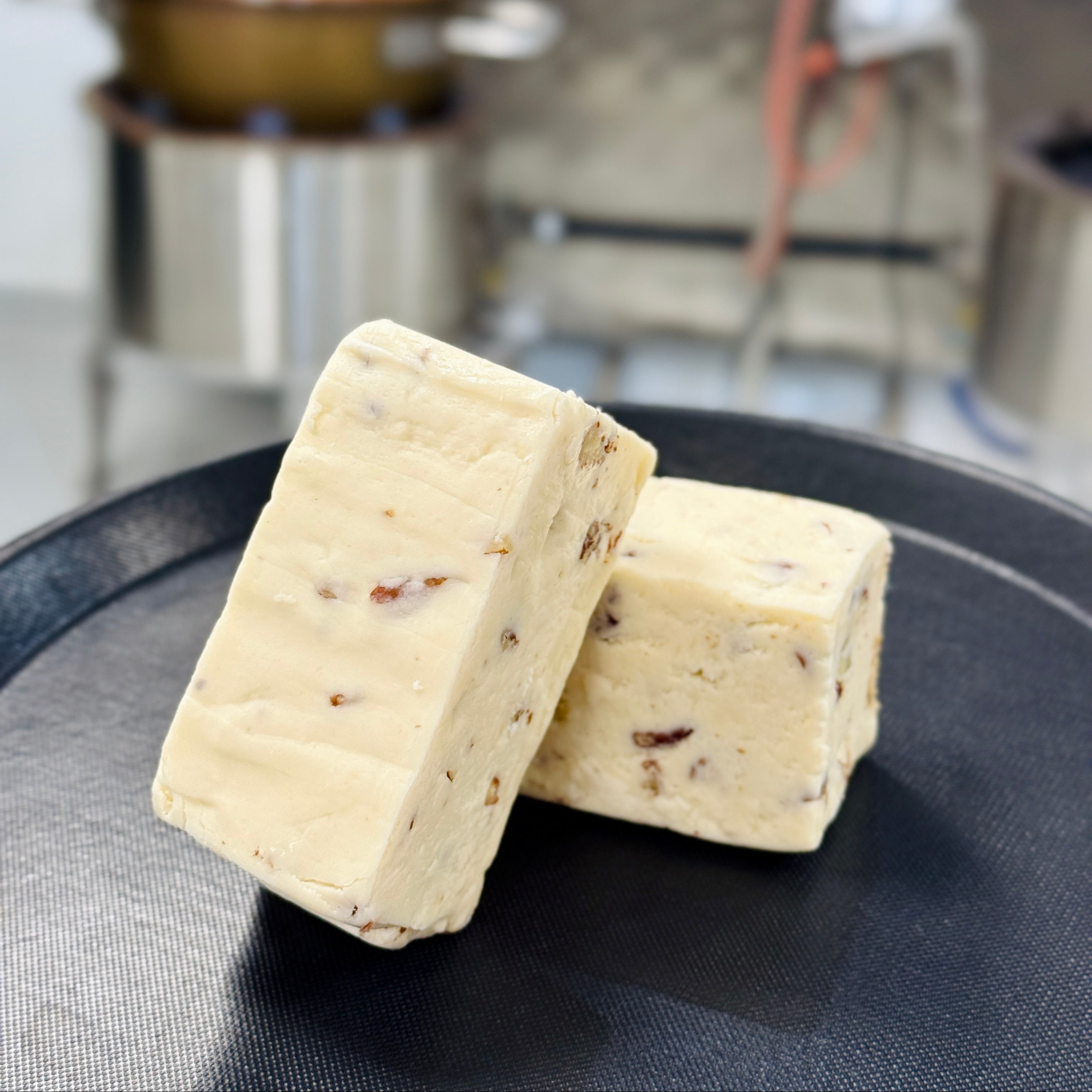 Two blocks of maple pecan fudge on a black plate in a kitchen setting.